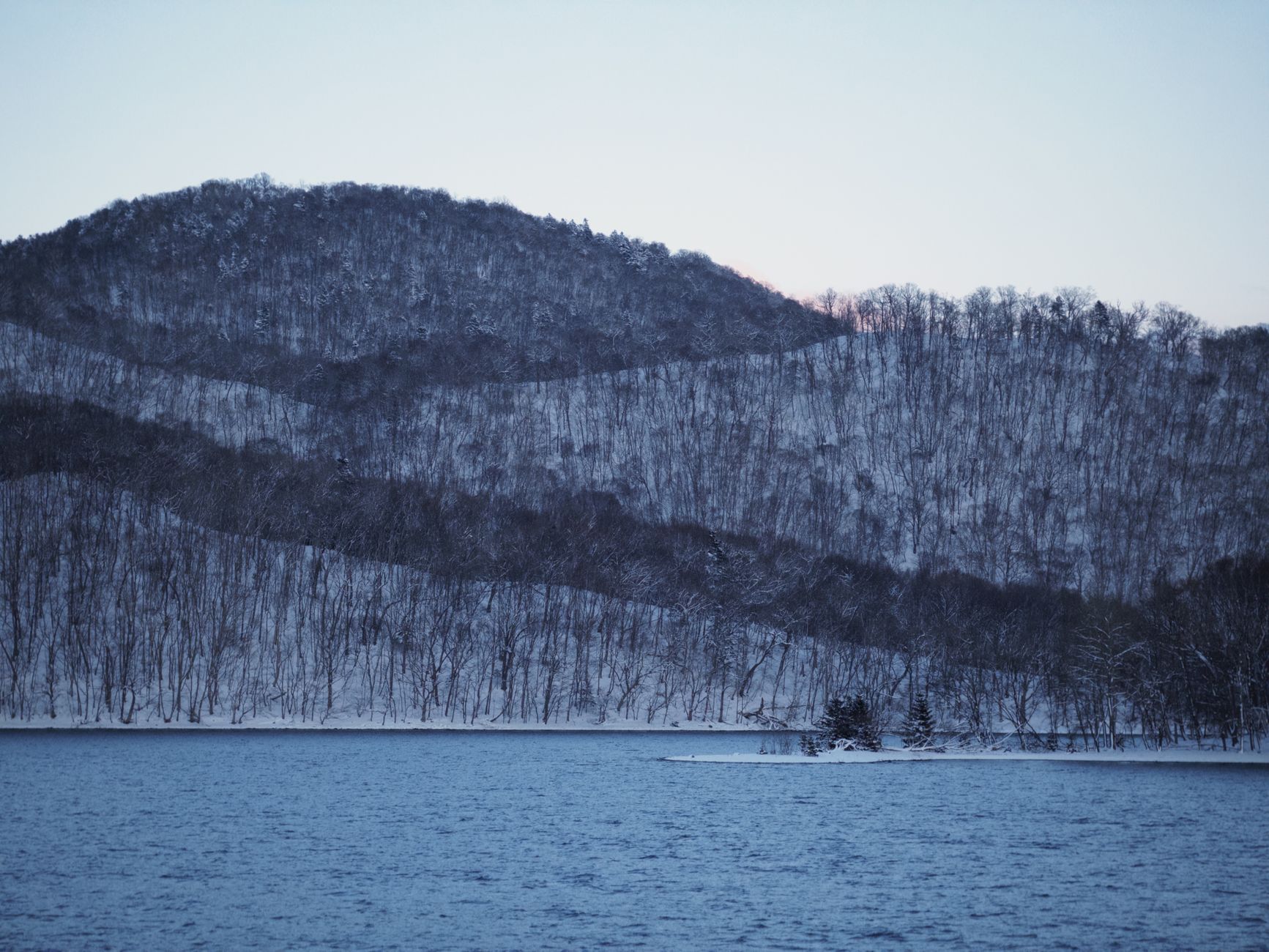 Lake Toya's flat, pewter-coloured water beneath Mount Usu, seen from an onsen ryokan terrace.