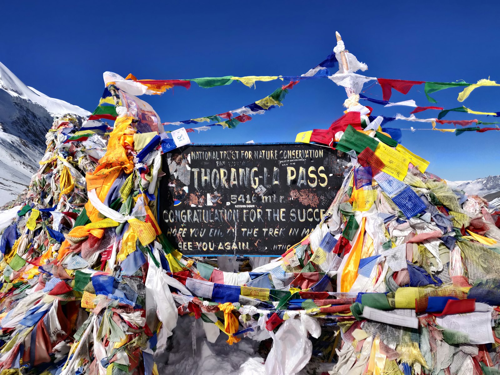 Prayer flags and trekkers at the Thorong La pass sign on the Annapurna Circuit