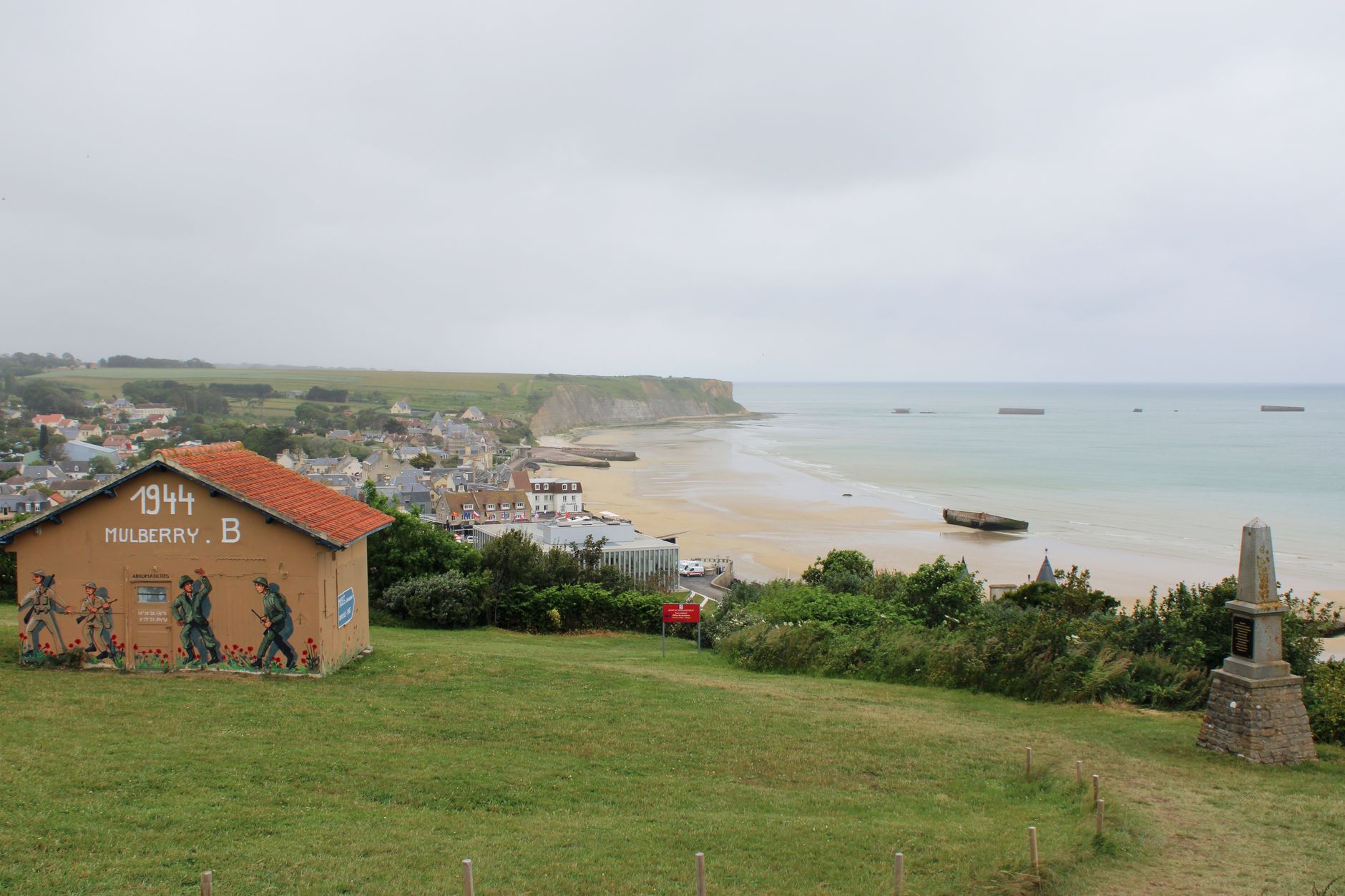 Rusting Mulberry harbor pontoons visible off Arromanches-les-Bains at low tide.