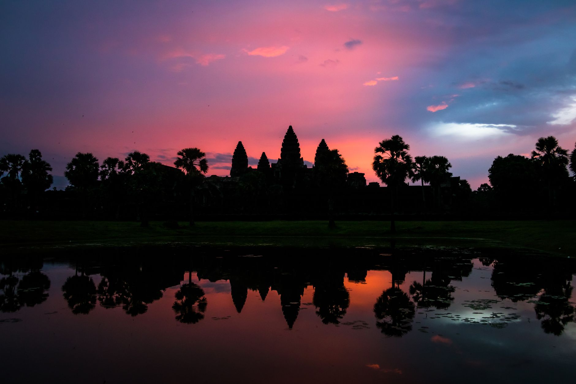 Silhouette of Angkor Wat's towers reflected in the lotus pond at sunrise