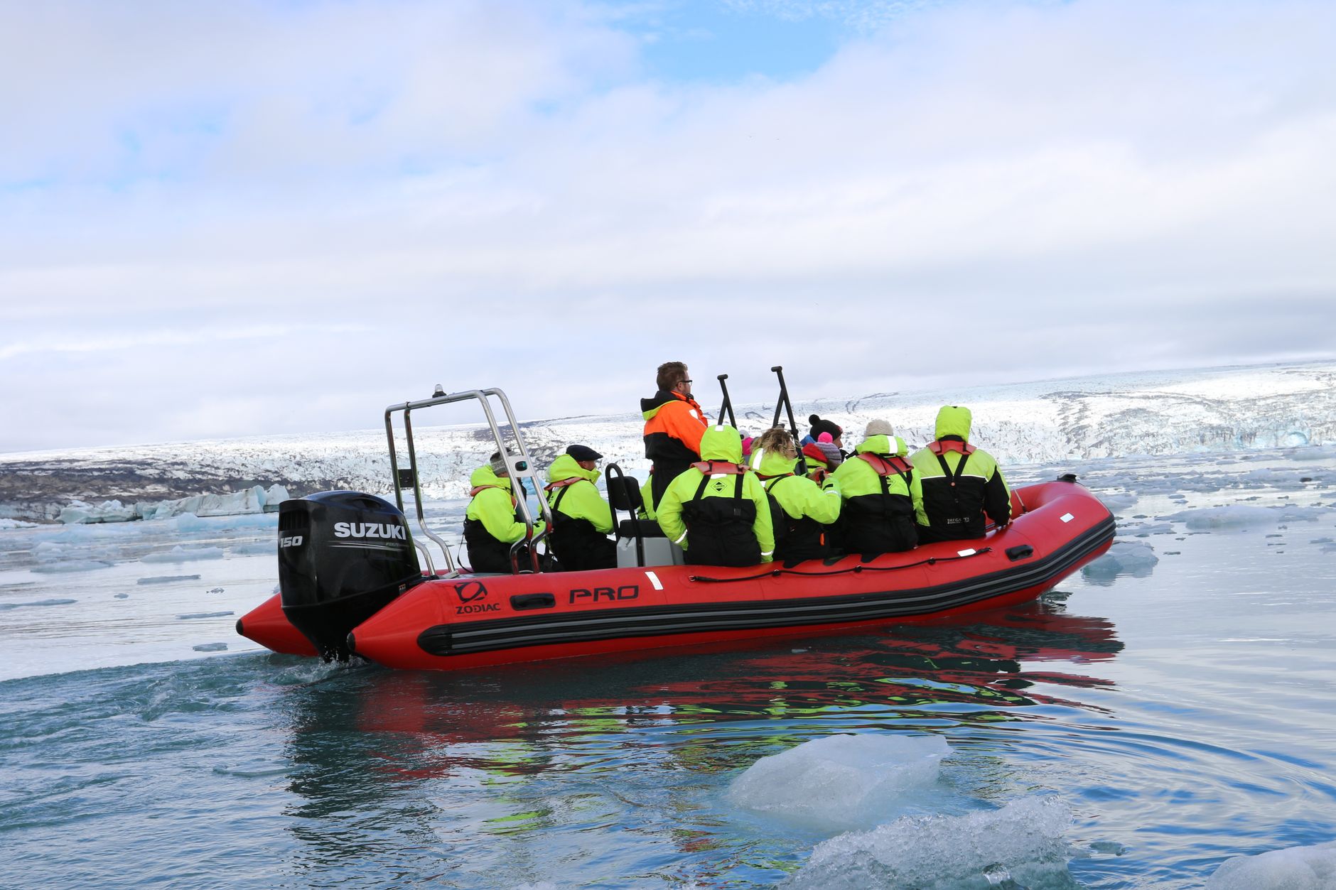Small rigid-hulled Zodiac boat full of passengers in bright life vests approaching glacial shoreline