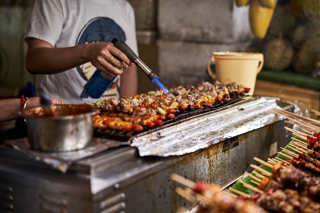 Street vendor at a Southeast Asian night market preparing grilled skewers