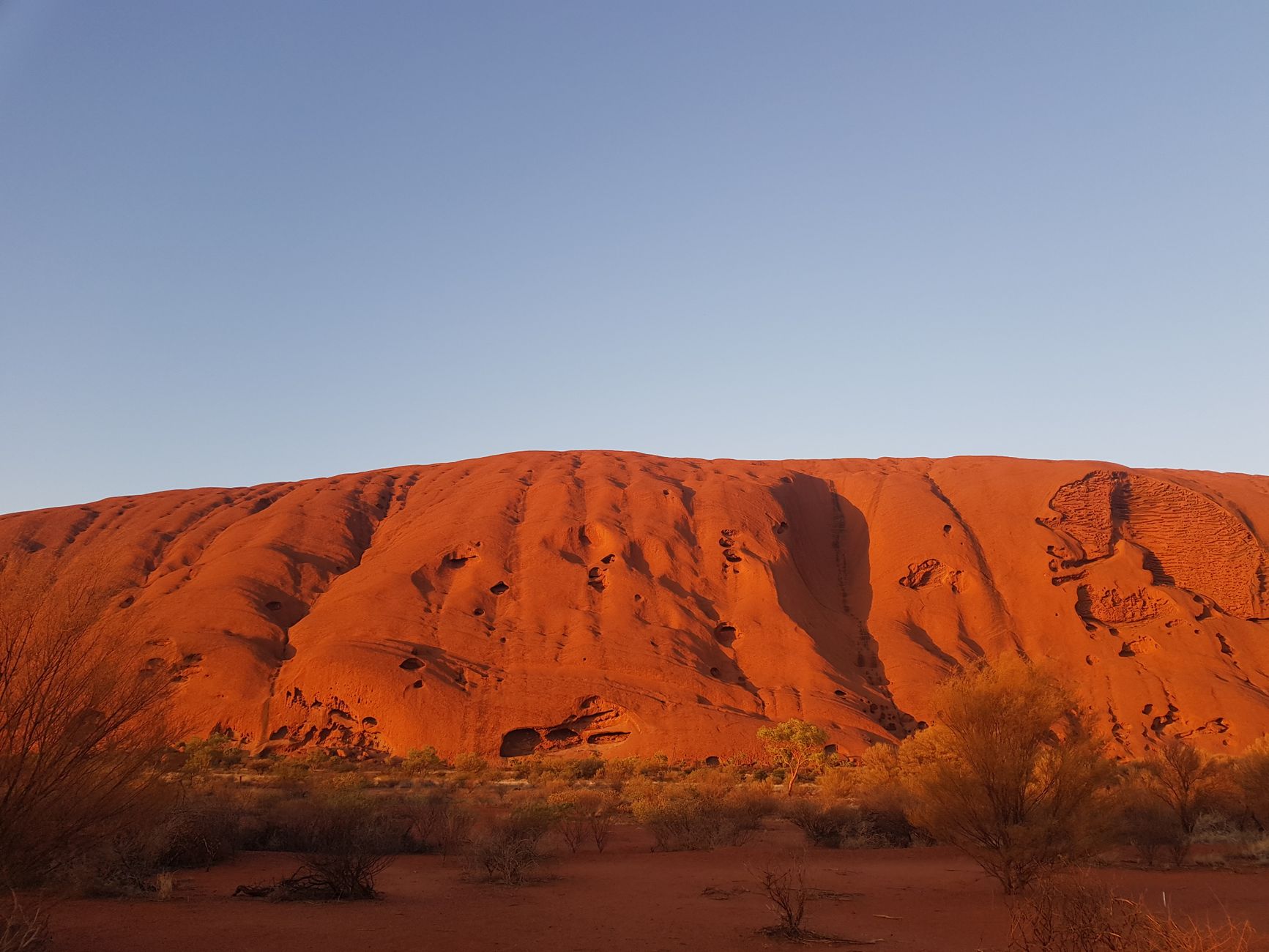 Sunrise light striking the red sandstone surface of Uluru along the base walking track