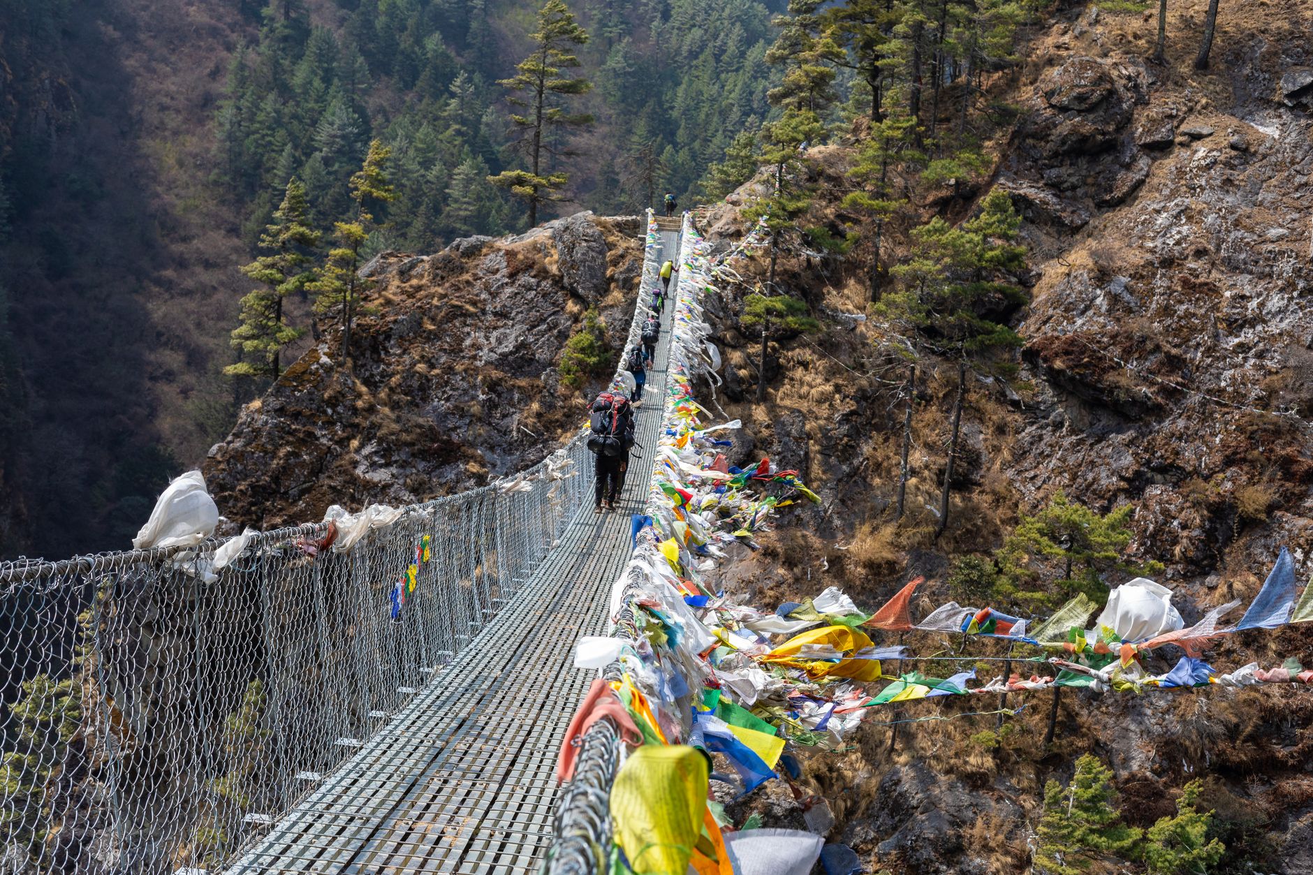 Trekkers crossing a suspension bridge over the Marsyangdi River with the Annapurna range behind