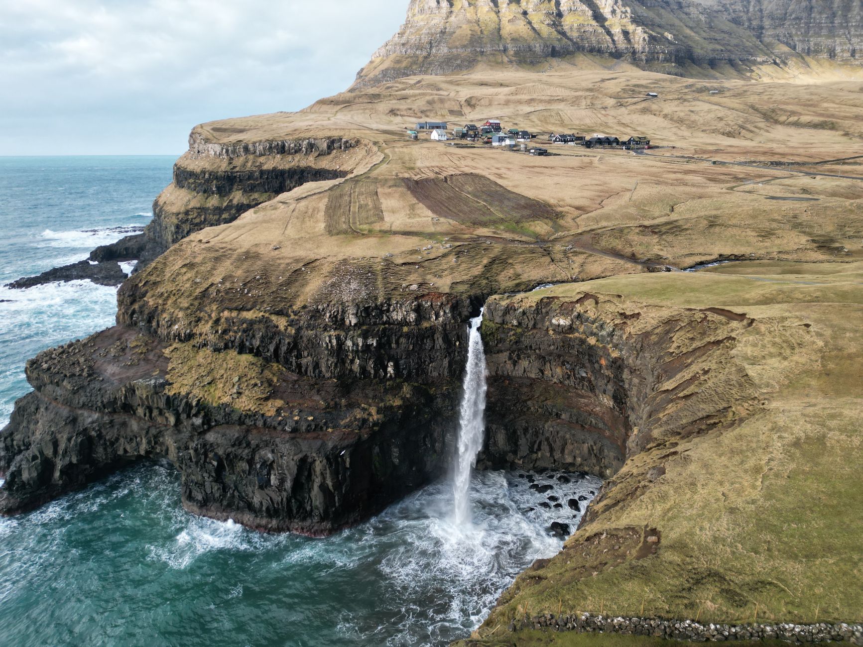Waterfall falling off a green cliff into the sea in the Faroe Islands