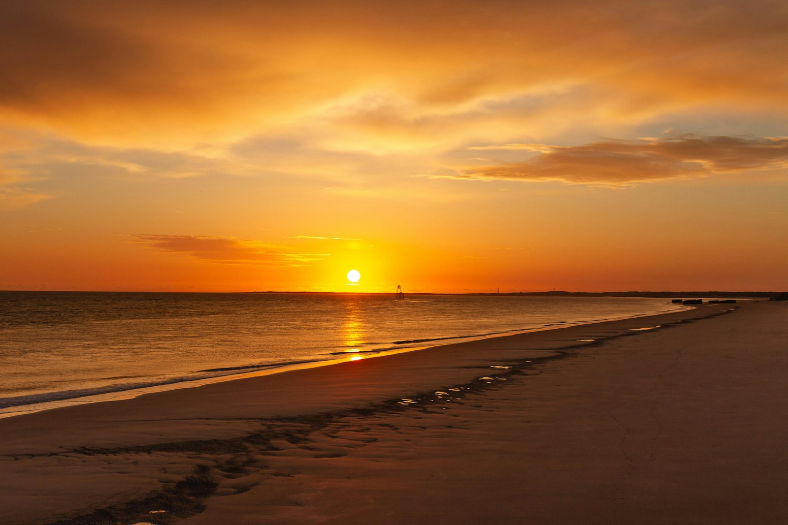 Wide sandy beach with calm blue-green water and colorful sky at sunset